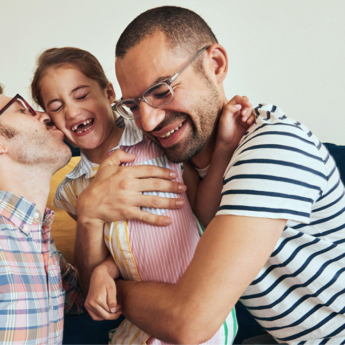 Two men hugging their daughter and smiling