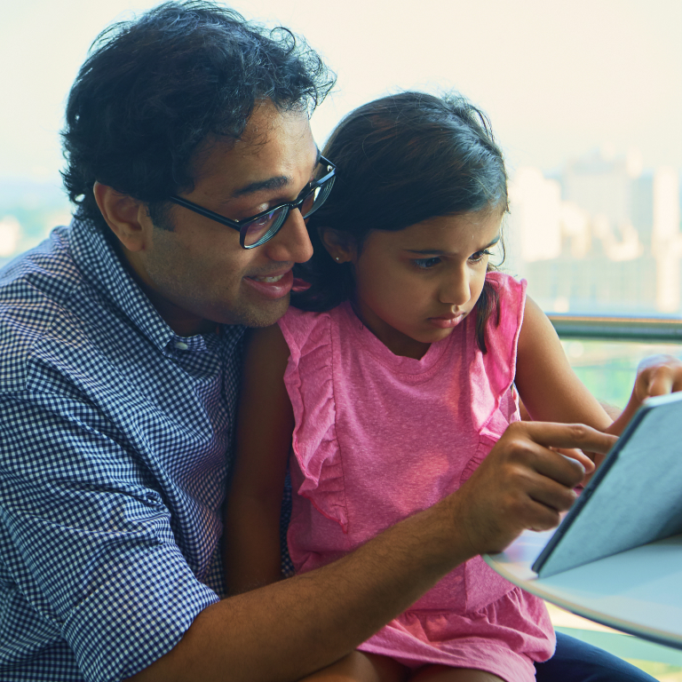 Father looking at a tablet with his daugher sitting on his lap