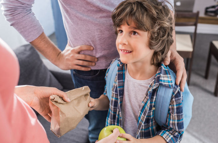 Young boy being handed his lunch and apple