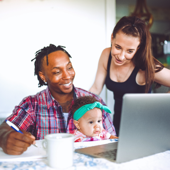 Man and woman looking at a laptop with their infant daughter