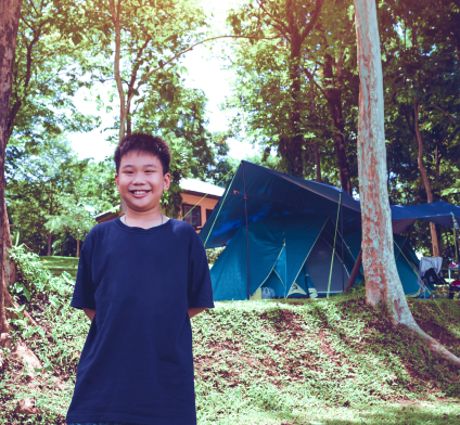 Asian Boy Smiling While Standing Outside Campsite in the Woods