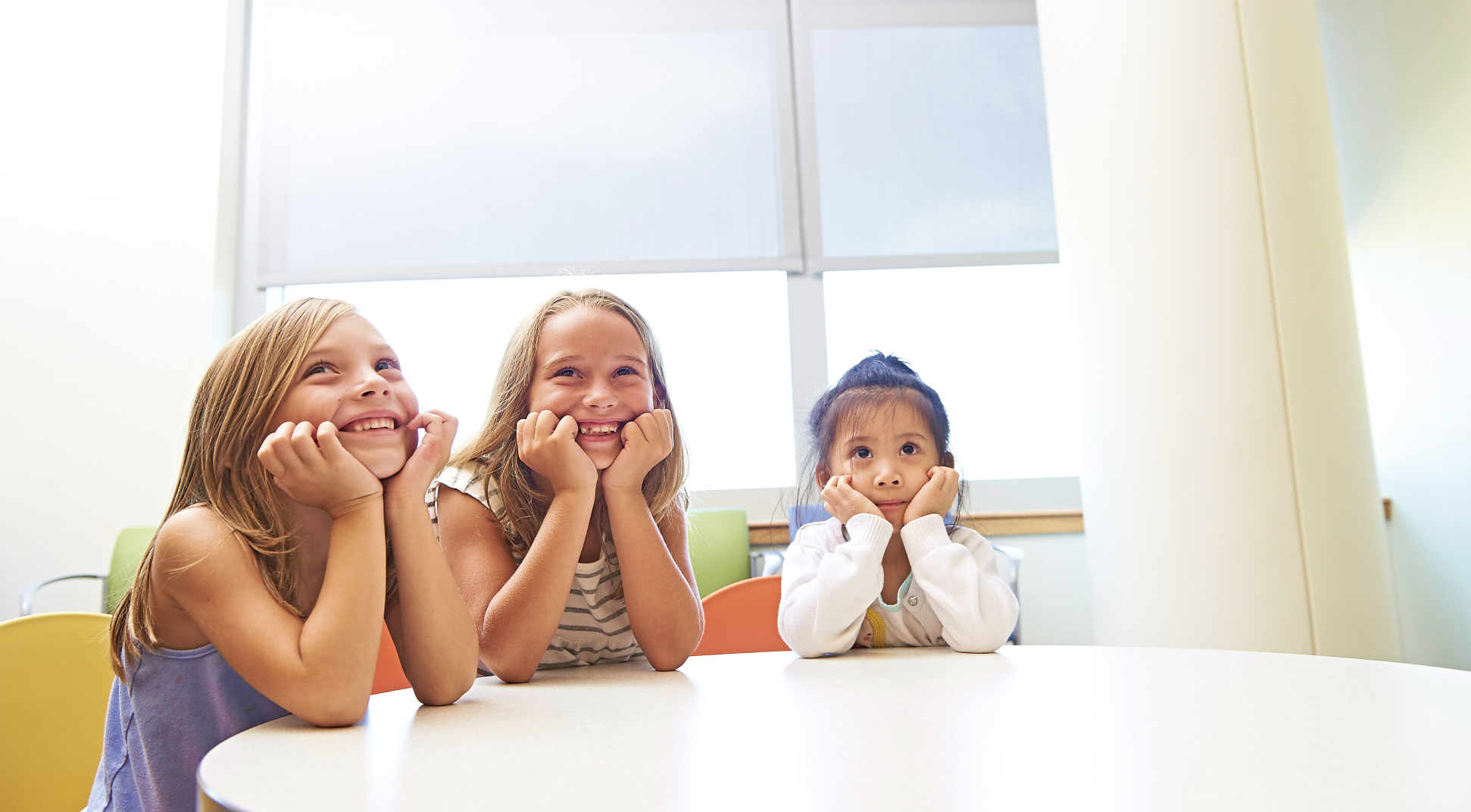 Three Young Girls Smiling While Sitting Around a Table