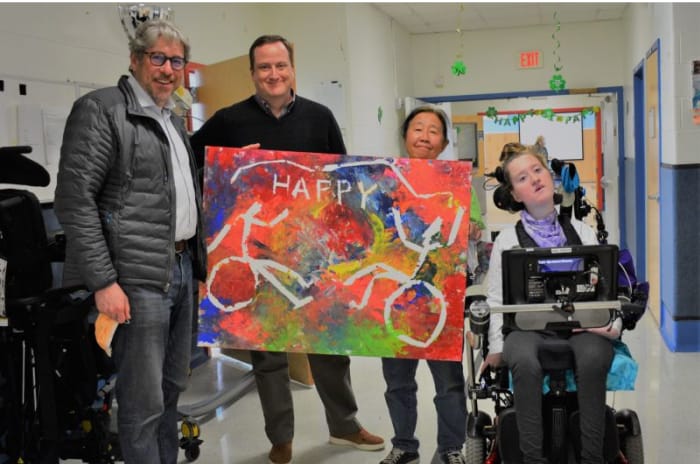 Three Adults Standing Next to Student with Cerebral Palsy in Wheelchair at School