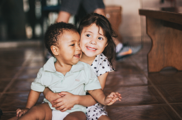 Young Girl Sitting on Floor Hugging Baby Boy